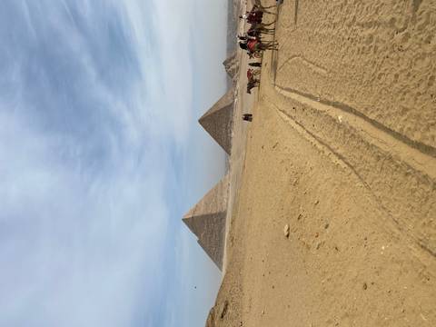 Expansive view across the Giza Plateau toward two pyramids with small groups of camel riders in the foreground.