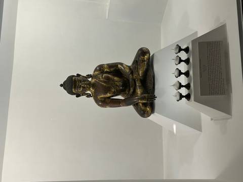 Bronze seated Buddha statue displayed in a minimalist museum case.