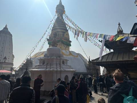 Crowds gather around Swayambhunath Stupa adorned with prayer flags in hazy light.