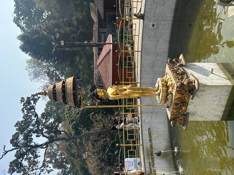 Golden statue of infant Buddha atop a pedestal fountain in a serene garden.