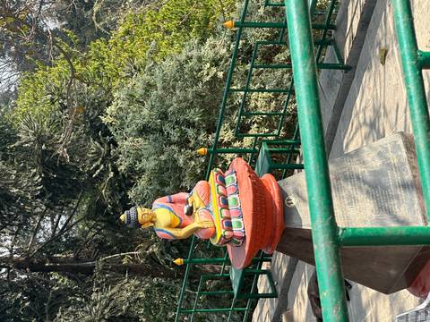 Colorful seated Buddha statue on a pedestal along a pathway lined with railings and greenery