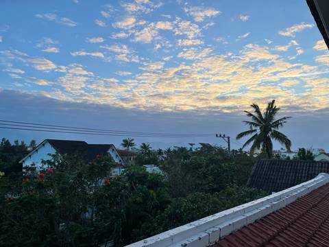 Early morning sky tinged with golden clouds above rooftops and palm trees.