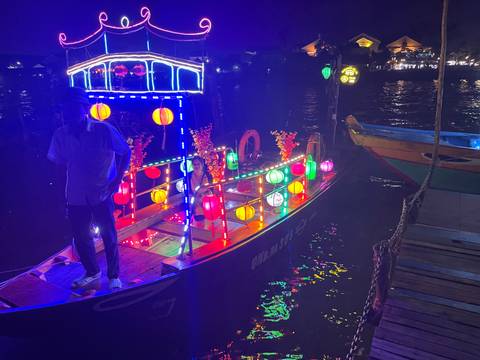 Vibrant night-time boat decorated with multicoloured lanterns on a river.
