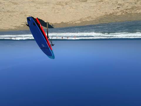 Surfboard planted upright on a sandy beach with gentle waves and swimmers under a clear blue sky.