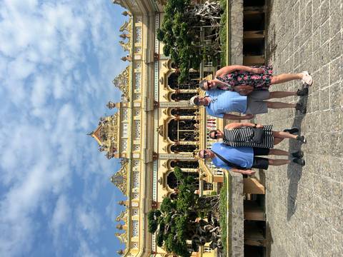 Four travelers pose in front of an ornate yellow pagoda under a bright blue sky.