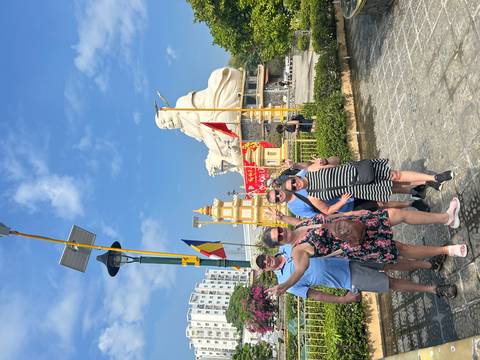 Happy group standing with arms raised beside a giant white seated Buddha and colorful flags.