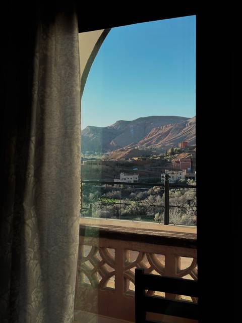 Mountain valley view through a hotel window and wrought-iron balcony railing at sunrise.