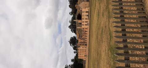 Historic sandstone penitentiary buildings across an open lawn under a cloudy Tasmanian sky.