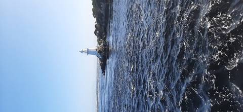 A solitary white lighthouse stands on a rocky islet amid choppy dark-blue waters.