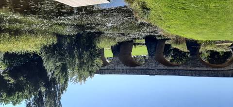Historic stone arch bridge crosses a reedy creek with lush green parkland beyond.