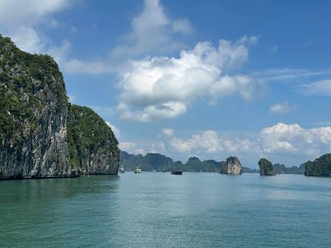 Tranquil jade waters weave between limestone karst islands under a sky dotted with white clouds in Halong Bay