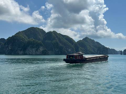 Long cargo barge glides across emerald waters framed by towering forested karst peaks