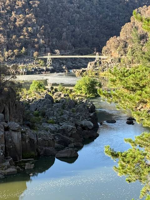 Rocky river gorges wind through bushland with a small suspension bridge in the distance.