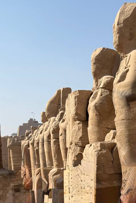 Row of weathered ancient ram-headed sphinx statues lining the avenue at Karnak Temple.