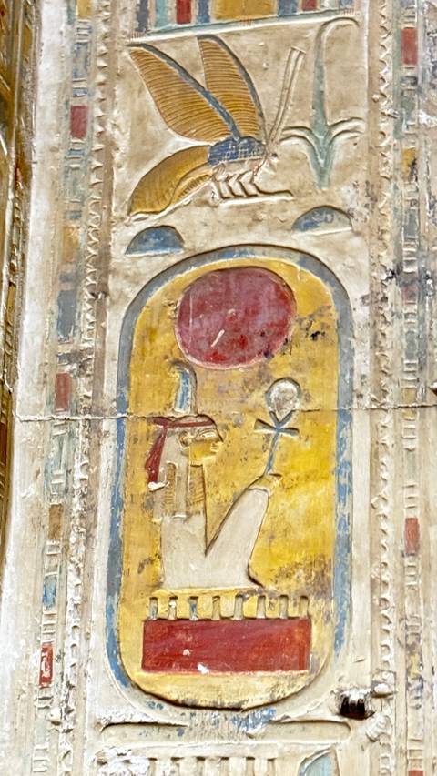 Close-up of colorful Egyptian wall relief showing a deity and an ankh beneath a red sun disc.