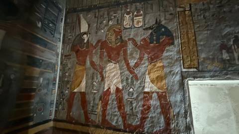 Wall painting of three Egyptian deities with animal heads in an ancient tomb chamber.