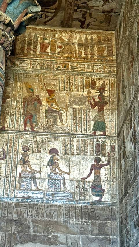 Vibrant wall panel with seated deity and hieroglyphic registers inside Egyptian temple.