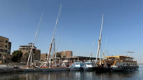 Row of traditional sailboats docked along the Nile under clear blue sky.