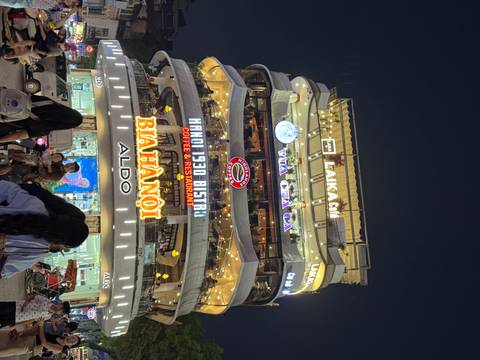 Night close-up of Hanoi's iconic round corner building glowing with neon restaurant signs.