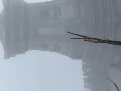 Fog-shrouded stone monument barely visible in thick mist on a mountaintop.