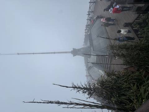 Visitors wander a mist-covered viewing deck and flagpole high in the mountains.