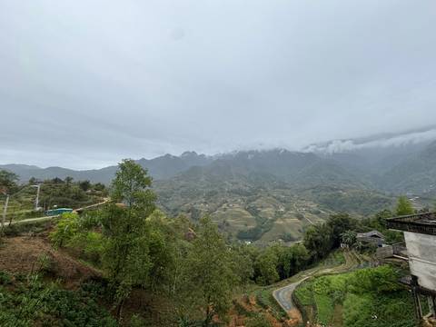 Overcast panorama of misty mountains and patchwork valleys dotted with small farms.