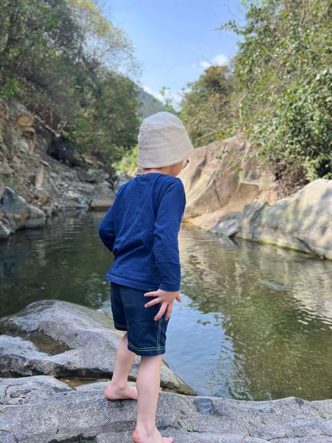 Child wearing bucket hat observing a calm rocky creek in a forested area.