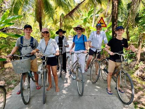 Group of travelers on bicycles along shaded rural path bordered by lush palms in Mekong Delta.