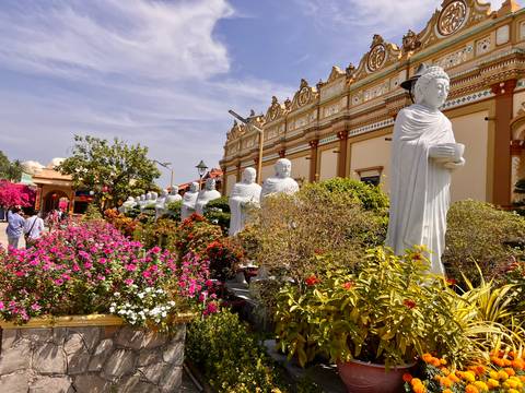 Colorful garden with blooming flowers and a row of white Buddhist statues at ornate temple complex.