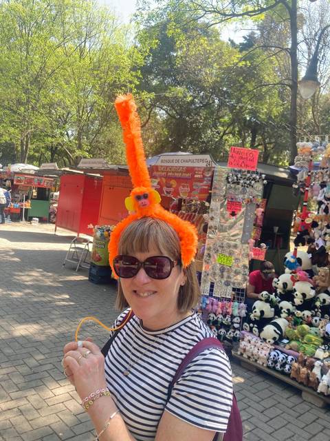 Woman wearing a playful orange monkey headband smiles in a bustling outdoor market stall area.