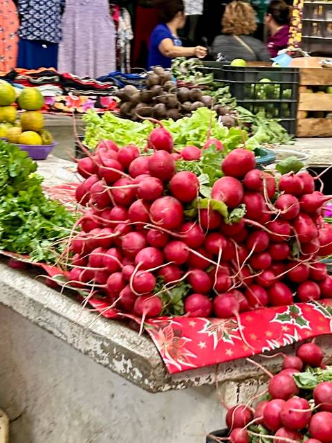 Pile of freshly harvested red radishes with leafy greens displayed at a market stall.