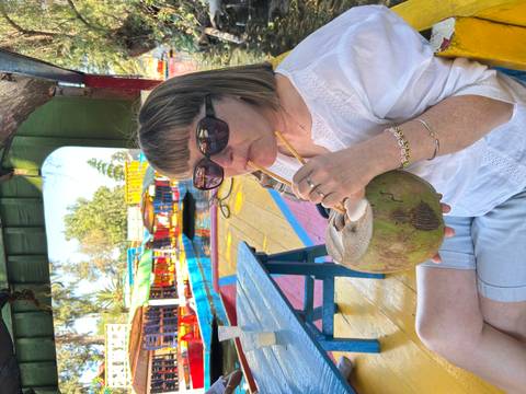 Woman sipping coconut water on a colorful trajinera boat floating through Xochimilco canals.