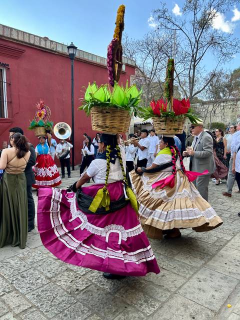 Traditional Oaxaca parade with women balancing flower baskets on their heads accompanied by musicians.