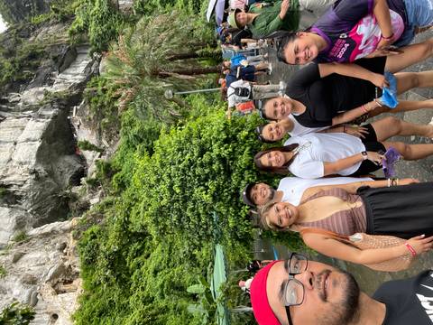 Smiling group poses beneath towering limestone cliffs and lush greenery near Halong Bay.