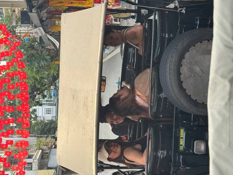 Friends look back and smile while seated in an open-top jeep driving through Hanoi streets.