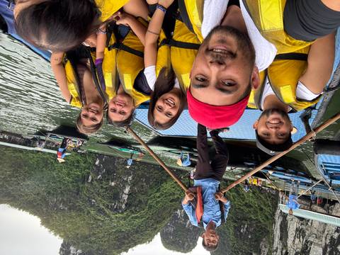 Group wearing yellow lifejackets smiles on a rowing boat amid the limestone pillars of Halong Bay.