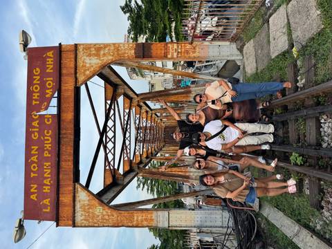 Friends pose on the rust-colored Long Biên railway bridge, arms raised in celebration.