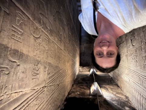 Visitor inside a narrow hieroglyph-covered corridor within an ancient Egyptian temple.