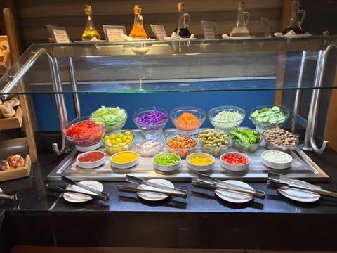 Second angle of a vibrant salad station showcasing lettuce, olives, peppers, and dressings.