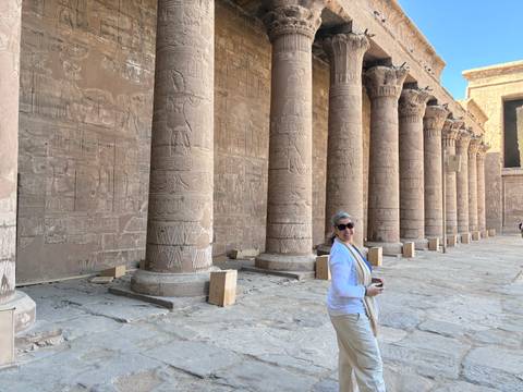 Visitor smiles while walking past intricately carved sandstone columns in an ancient Egyptian temple courtyard.