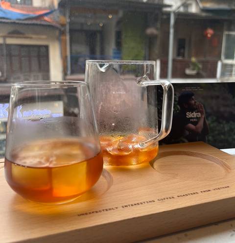 Close-up of chilled amber coffee drinks in glassware on a wooden tray at a Hanoi café window.