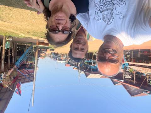 Happy tourists taking a selfie on a sun-lit street of elevated wooden houses in a floating village.