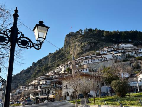Historic hillside town of white-washed Ottoman houses beneath a rocky citadel and blue sky.