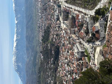 Aerial view of a sprawling city surrounded by green valleys and snowy mountain peaks.
