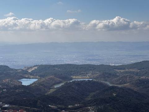 Wide vista of Tirana valley with lakes and cityscape beneath rolling mountain ranges and cloud banks.