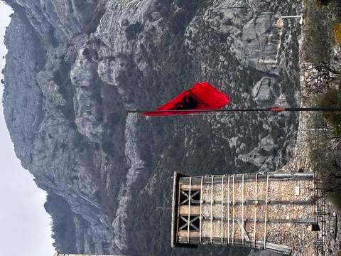 Albanian flag waving before rugged grey mountains and a stone tower structure.