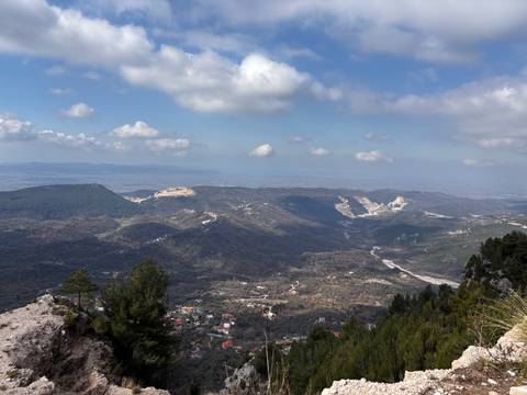 Wide panoramic view of a green valley and distant plains seen from a high mountain ridge on a bright day.