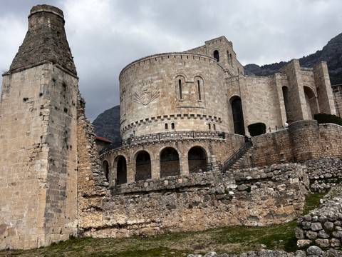Impressive stone fortress and circular tower with arched galleries rising above ancient walls under a grey sky.