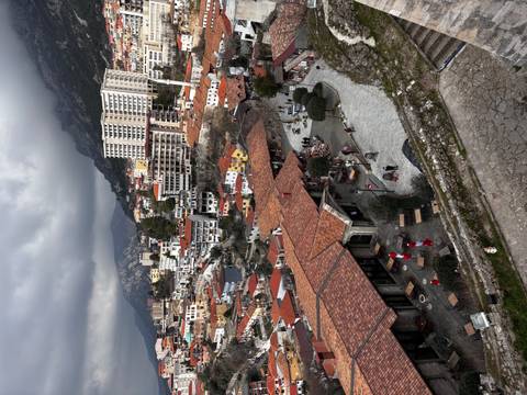 High vantage view over tiled rooftops, winding streets and surrounding mountains beneath dramatic clouds.