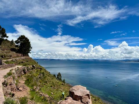 A coastal trail skirts the deep blue waters of Lake Titicaca beneath a sky of dramatic clouds.
